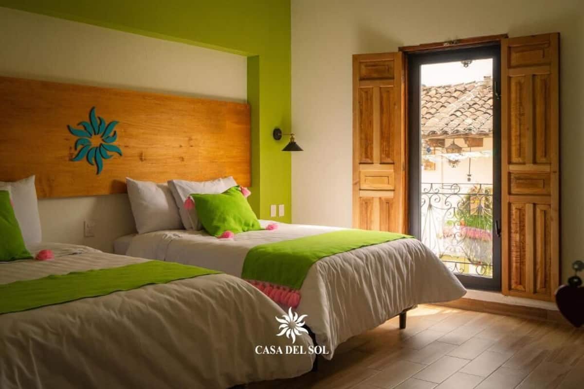 Une chambre d’hôtel avec deux lits, une tête de lit en bois, un mur d’accent vert, un balcon avec vue et une porte à panneaux de bois.