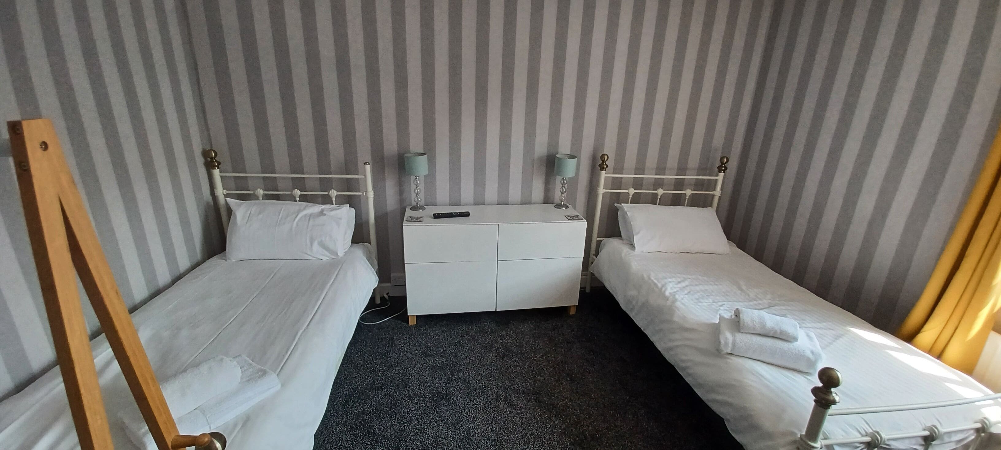 Une chambre avec deux lits simples, une petite commode blanche et un chevalet en bois.