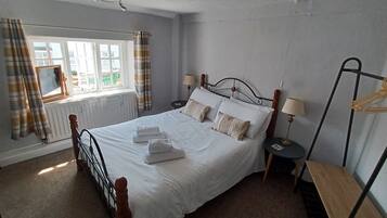 A neatly made bed with pillows and towels, a bedside table with a lamp, a window with curtains, and a radiator.