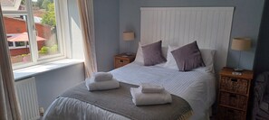 A neatly made bed with pillows, a bedside table with a lamp, and a window with curtains. - Winchester Arms (Taunton)