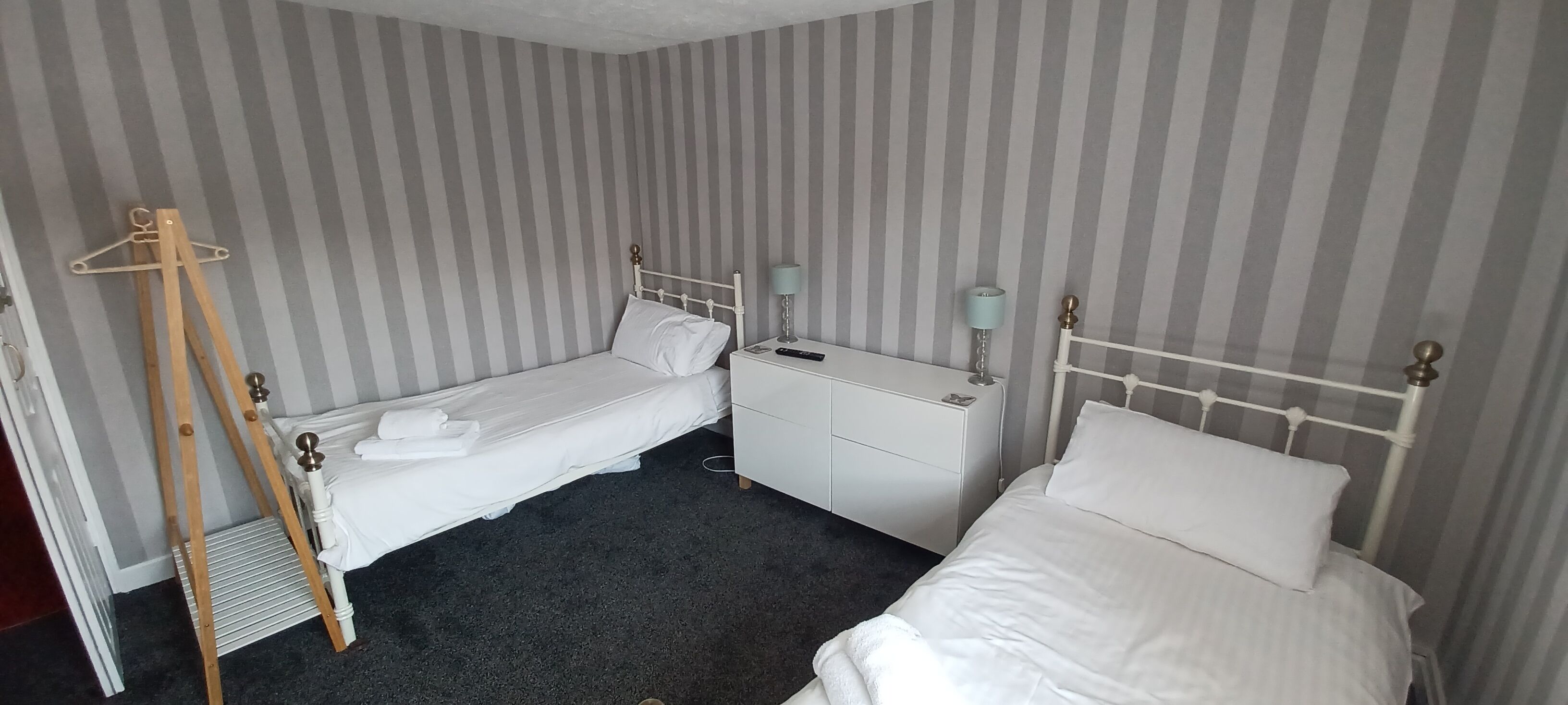 Una habitación con dos camas individuales, un pequeño aparador y un caballete de madera.