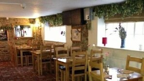 A restaurant with wooden tables and chairs, stone walls, and a window with a plant. - Winchester Arms (Taunton)