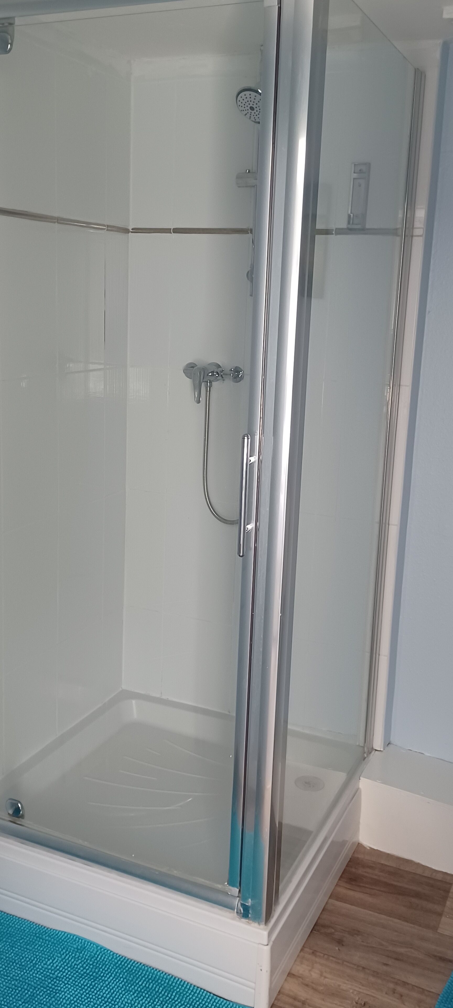 Un box de ducha con paredes de vidrio, un cabezal de ducha manual y un grifo de pared.