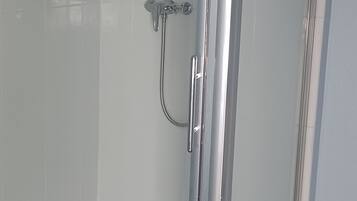 Un box de ducha con paredes de vidrio, un cabezal de ducha manual y un grifo de pared.