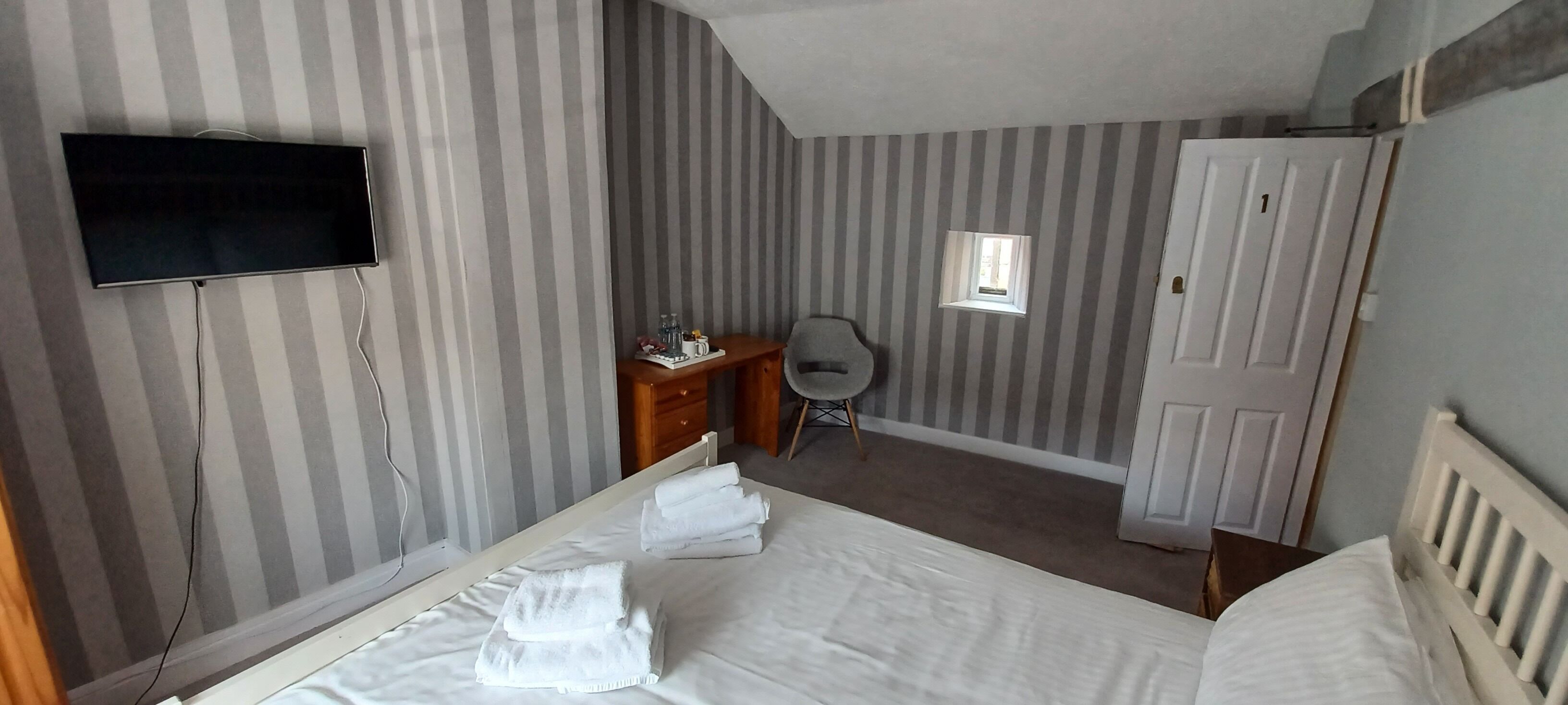 Et hotelværelse med en seng, et skrivebord, en stol, et fjernsyn og et vindue.