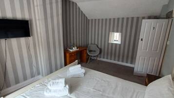 Et hotelværelse med en seng, et skrivebord, en stol, et fjernsyn og et vindue.