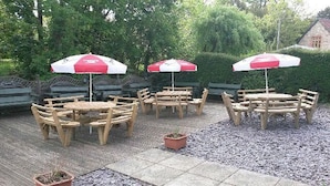 Outdoor wooden tables and benches with red and white umbrellas, surrounded by gravel and greenery. - Winchester Arms (Taunton)