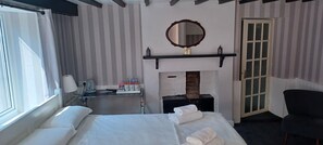 A hotel room with a bed, a desk with toiletries, a fireplace, and a mirror on the wall. - Winchester Arms (Taunton)