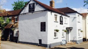A white building with a black sign, a chimney, and a signboard. - Winchester Arms (Taunton)