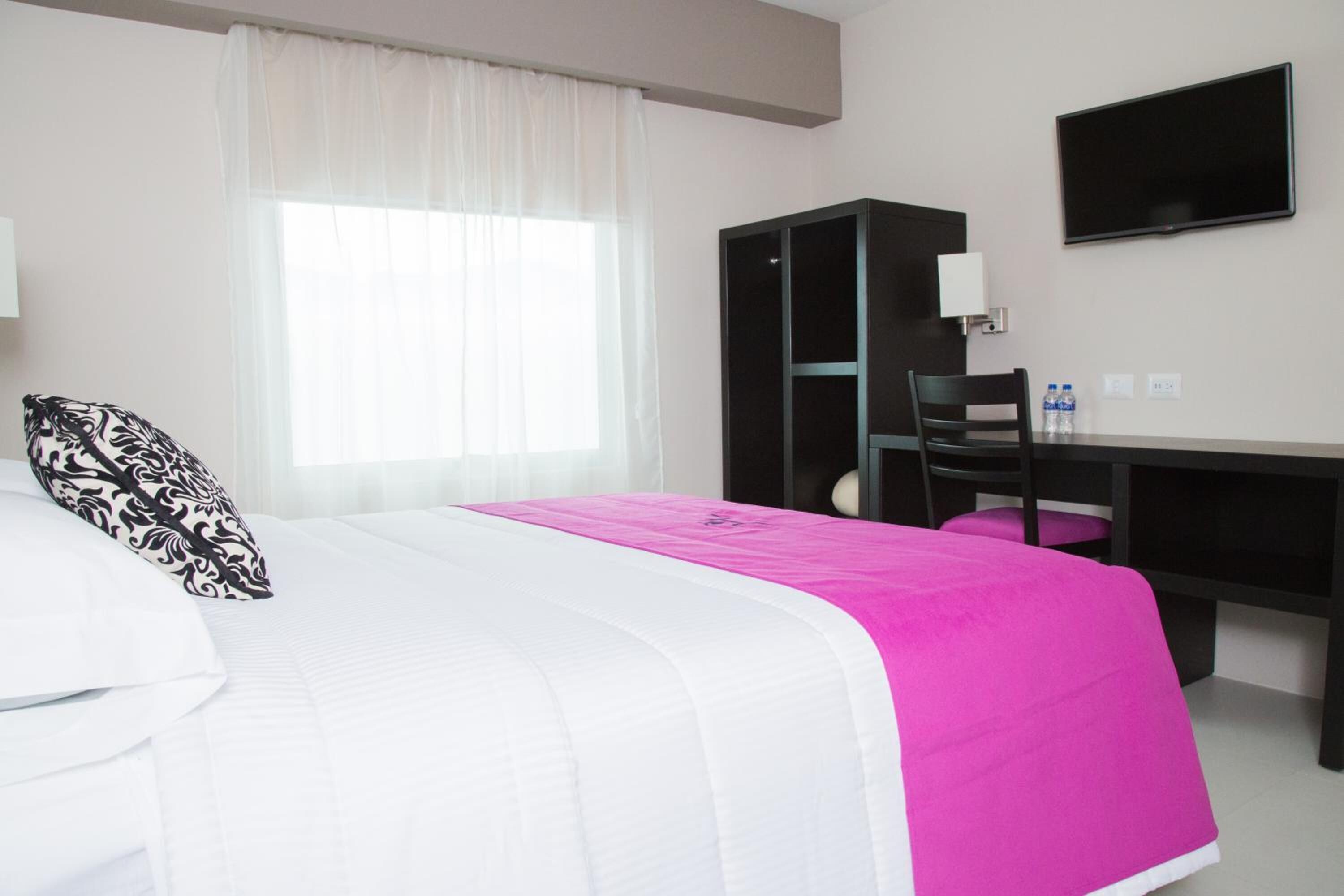 Una habitación de hotel con cama, escritorio, silla, televisor y armario.