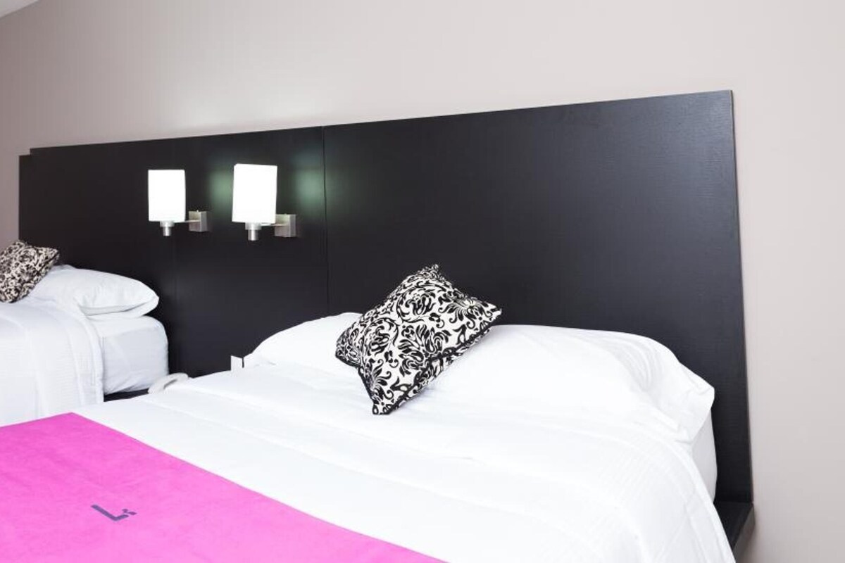 A hotel room with two beds, a desk, a chair, and a small table.