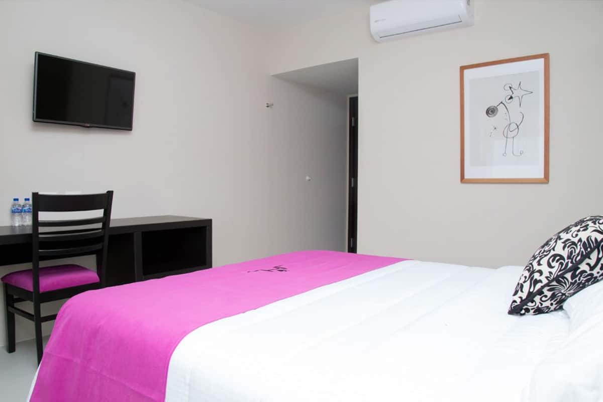 A hotel room with a bed, a desk, a chair, a television, and a framed picture on the wall.