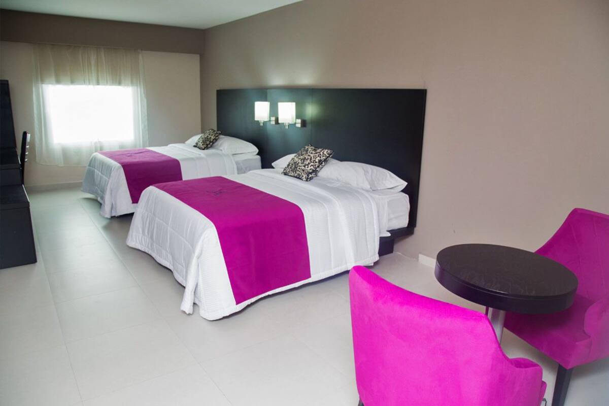 A hotel room with two beds, a small table, and a chair.