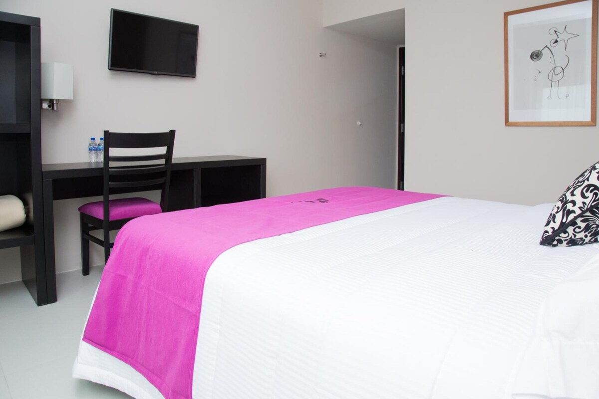 A hotel room with a bed, a desk, a chair, a television, and a framed picture on the wall.