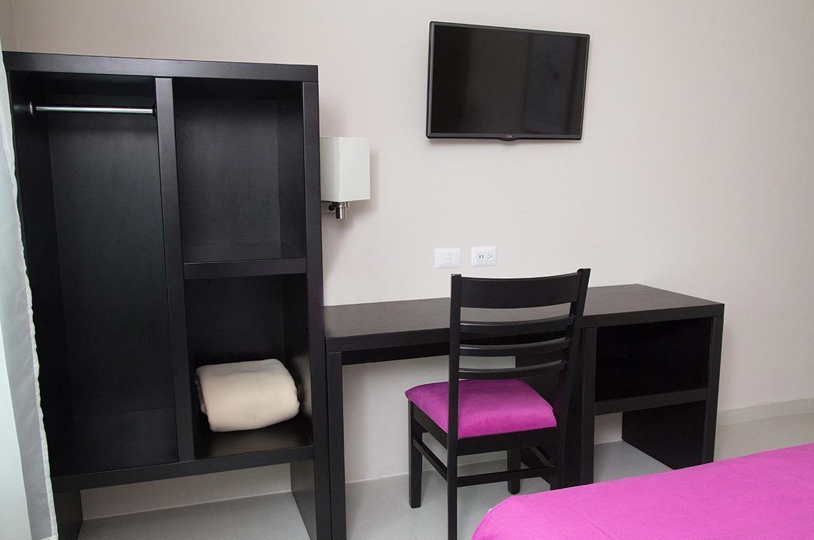 A room with a bed, a desk, a chair, a wardrobe, and a TV.