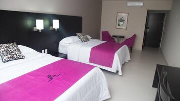 A hotel room with two beds, each with a white bedspread and a pink runner. There is a small table and a chair in the room.