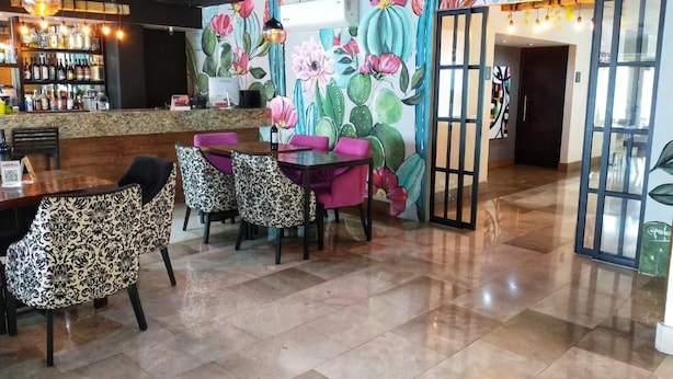 Un interior de restaurante con zona de bar, barra y comedor con sillas estampadas y una mesa.