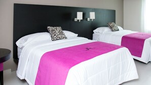 Dos camas con ropa de cama blanca y colchas rosadas, un cabecero negro y dos lámparas fijadas a la pared.
