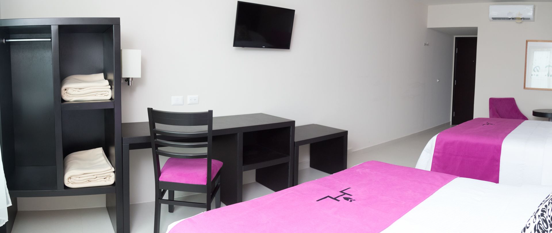 A hotel room with a bed, a desk, a chair, a wardrobe, and a television.