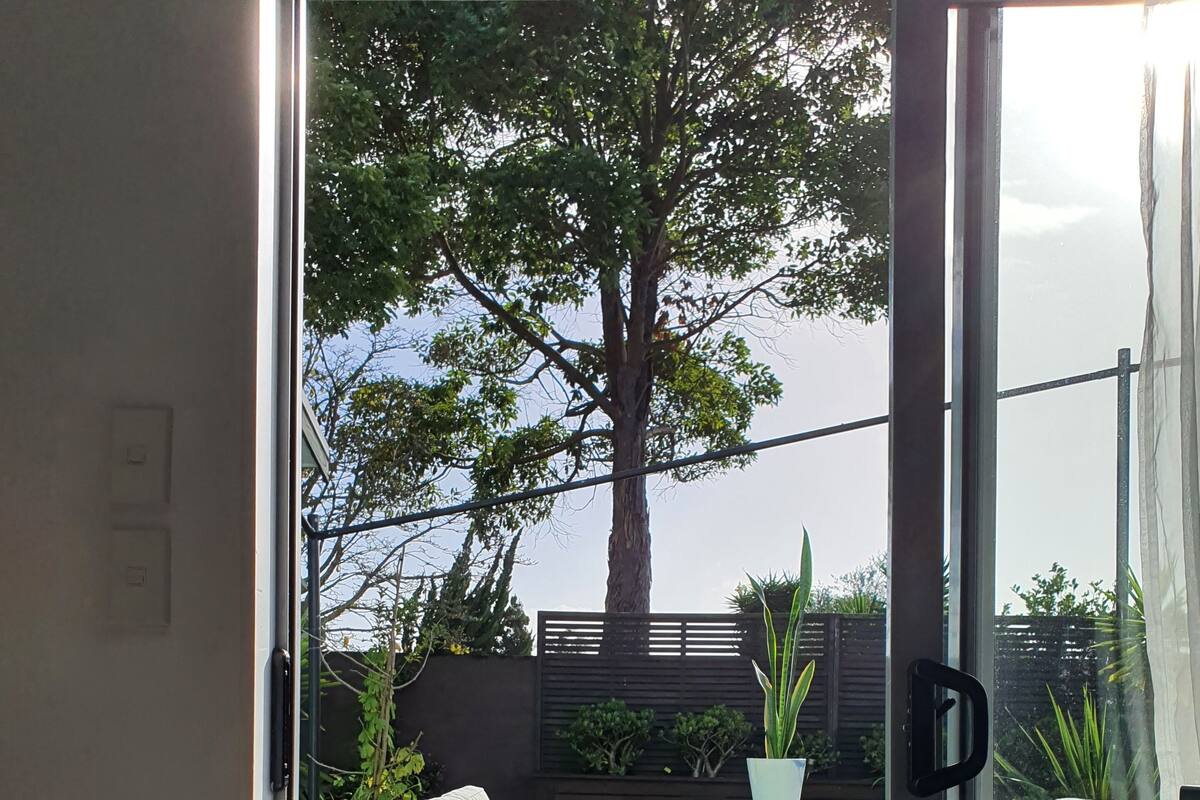 Una puerta corrediza de vidrio que da a un patio exterior con muebles de mimbre y un árbol grande.