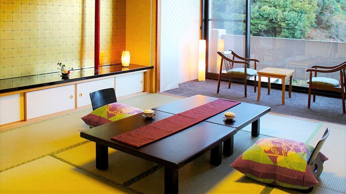 Ein traditioneller japanischer Raum mit Tatami-Boden, einem niedrigen Tisch mit Kissen und Blick durch große Fenster.