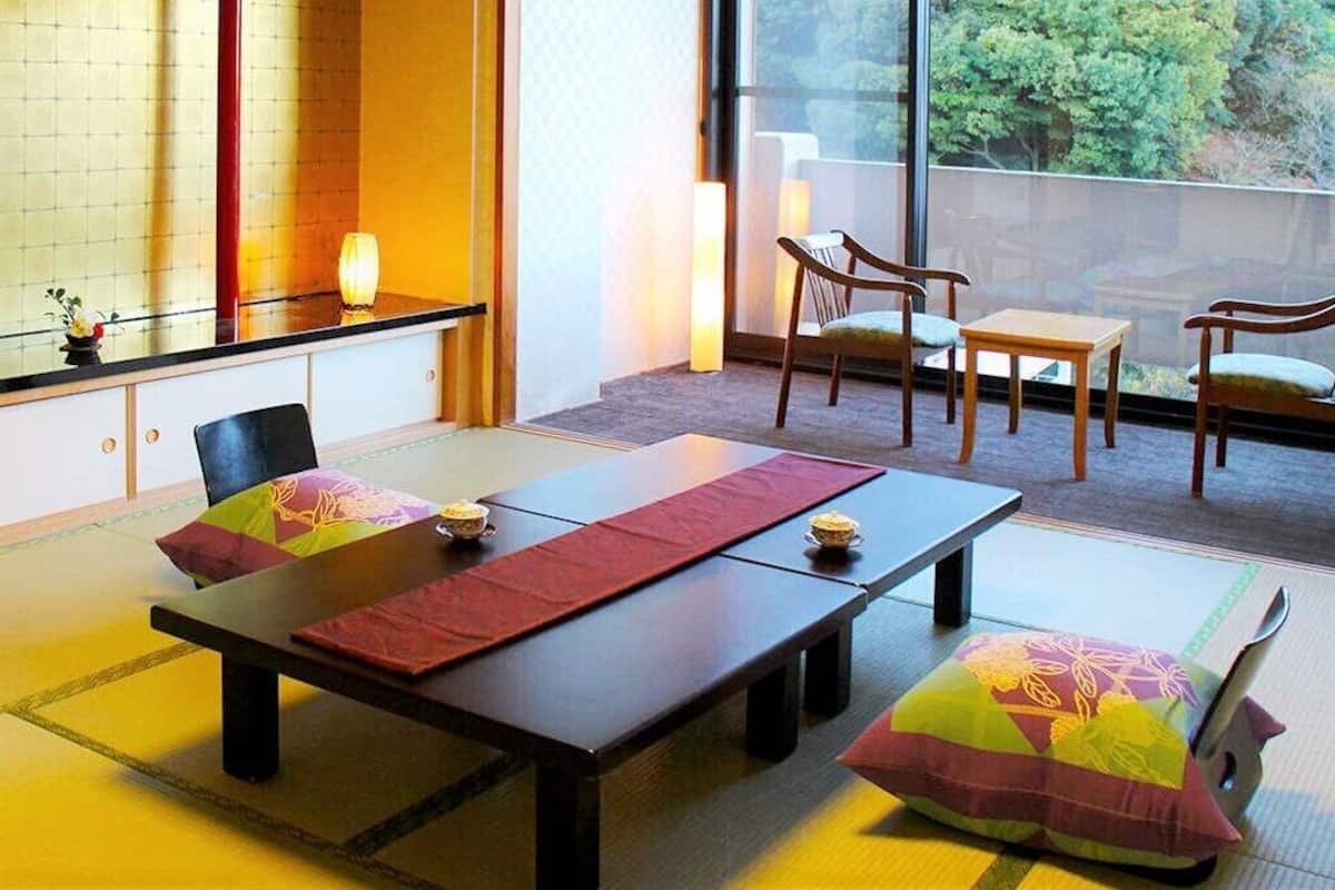 Une pièce de style japonais traditionnel, avec un sol recouvert de tatamis, une table basse avec des coussins et une vue dégagée grâce à de grandes fenêtres.