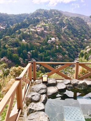Una terraza de madera con una fuente de piedra y vistas a un paisaje montañoso.