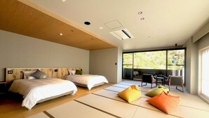 Een moderne hotelkamer met twee bedden, tatami matten, een zithoek met stoelen en grote ramen met uitzicht op de omgeving.