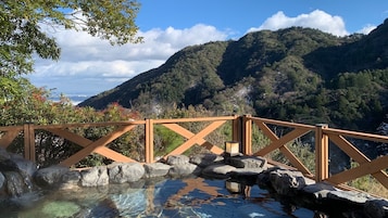 Terraza de madera con vistas a un manantial termal y montañas al fondo.