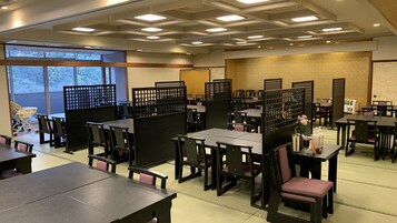 Un restaurante con varias mesas y cabinas, separado por paneles negros, y vistas a árboles a través de amplias ventanas.
