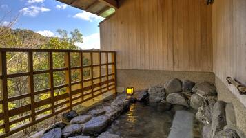 Un onsen japonés tradicional con interior de madera, manantial termal de piedra y valla de madera con vistas a un paisaje natural.