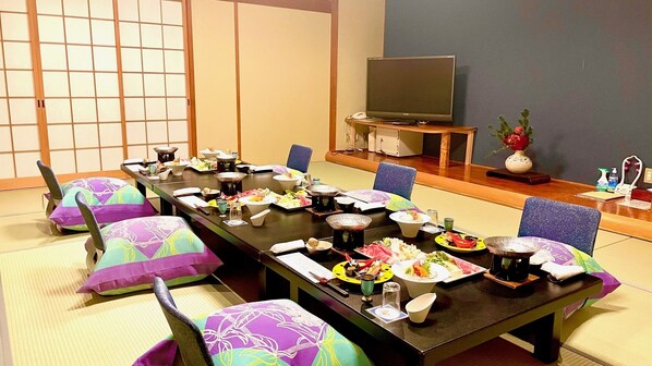 Et traditionelt japansk rum med tatamimåtter, et lavt bord med forskellige retter, og et fjernsyn på et stativ.