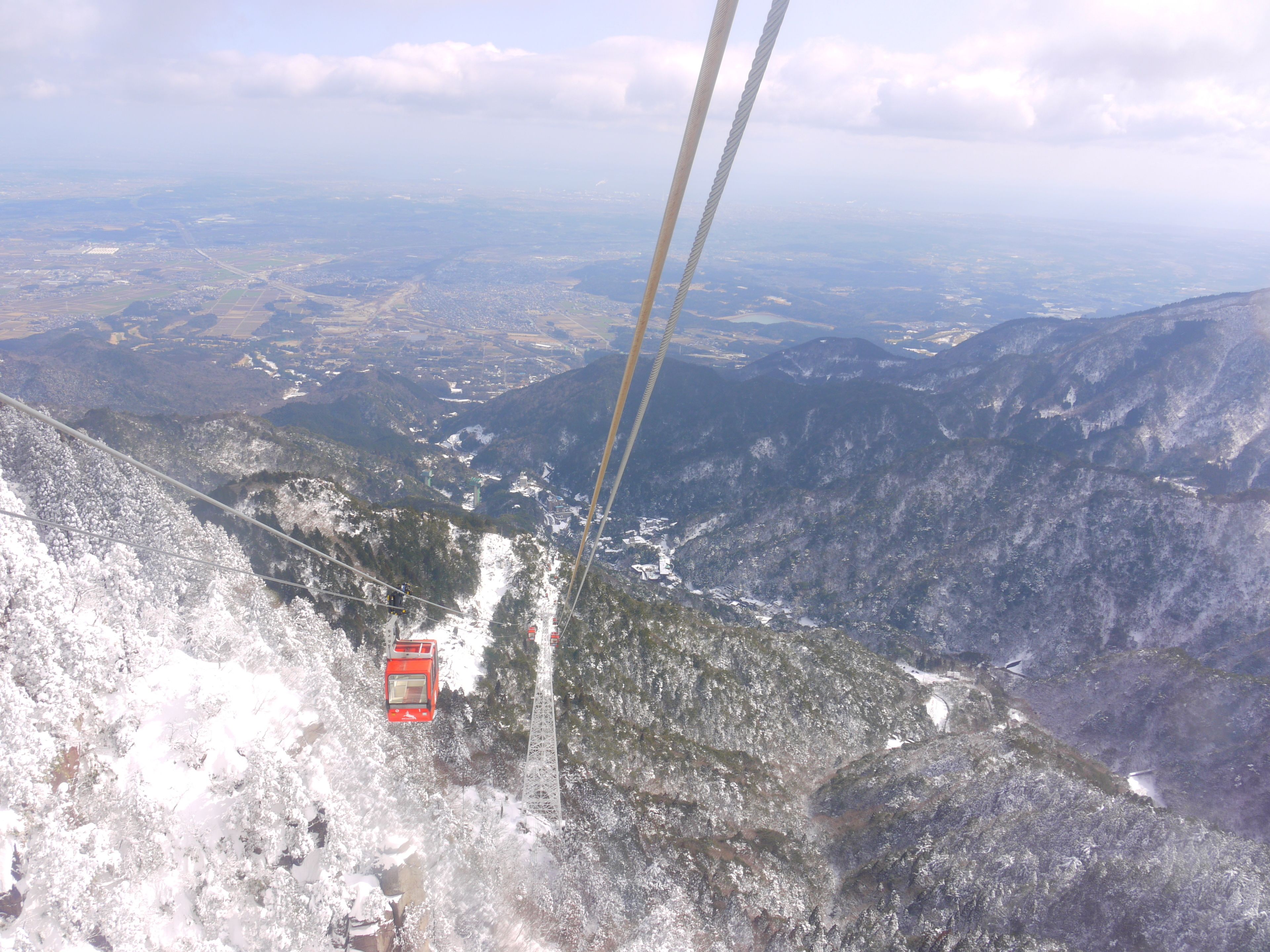 A cable car system in a mountainous area with snow-covered terrain and distant views of a valley.