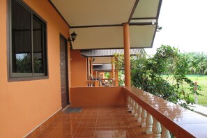 A covered balcony with a tiled floor, a railing, and a view of a garden. - El Greco Bungalows (Ko Lanta)
