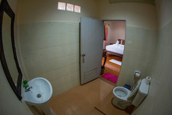 Une salle de bain équipée d’un lavabo, de toilettes et d’une porte donnant sur une chambre.