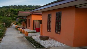Un chemin mène à une rangée de bâtiments aux façades orange, dotés de grandes fenêtres, et bordé d’un sentier en pierre.
