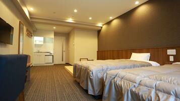 A hotel room with two beds, a desk, a chair, a TV, and a kitchenette.