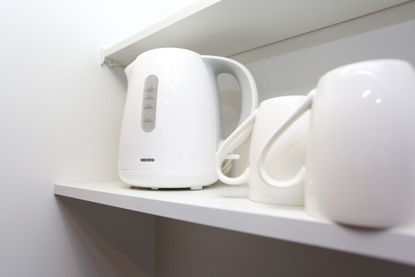 A white kettle and two white mugs on a white shelf.