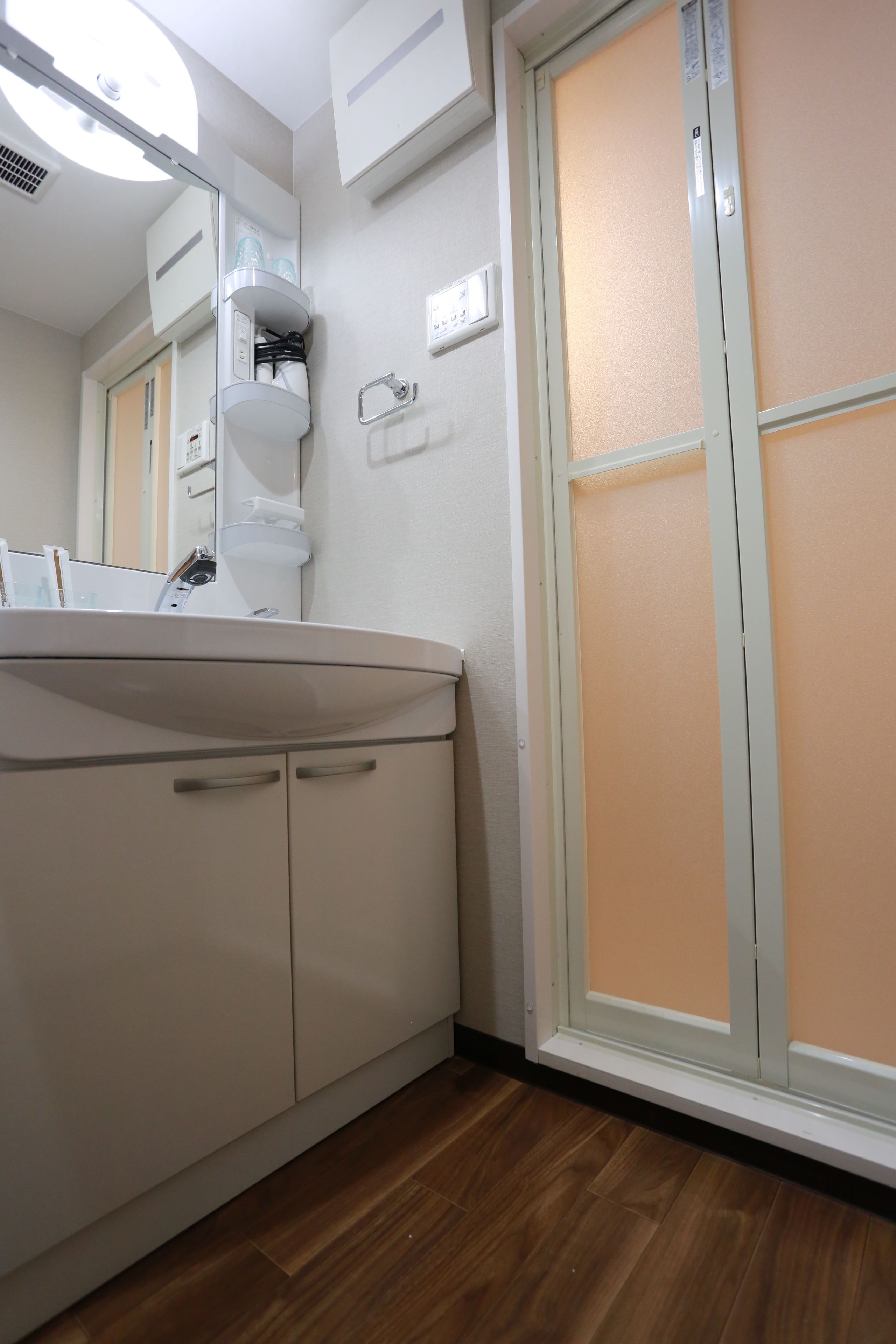 A bathroom with a white sink, mirror, and cabinets. There is a window with frosted glass panels and a wooden floor.