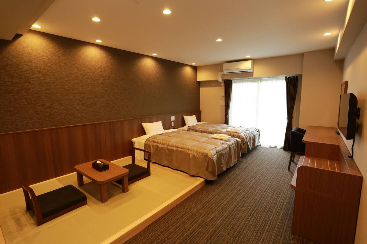 Hotelkamer met twee bedden, een bureau, een stoel, een televisie en een raam met gordijnen.