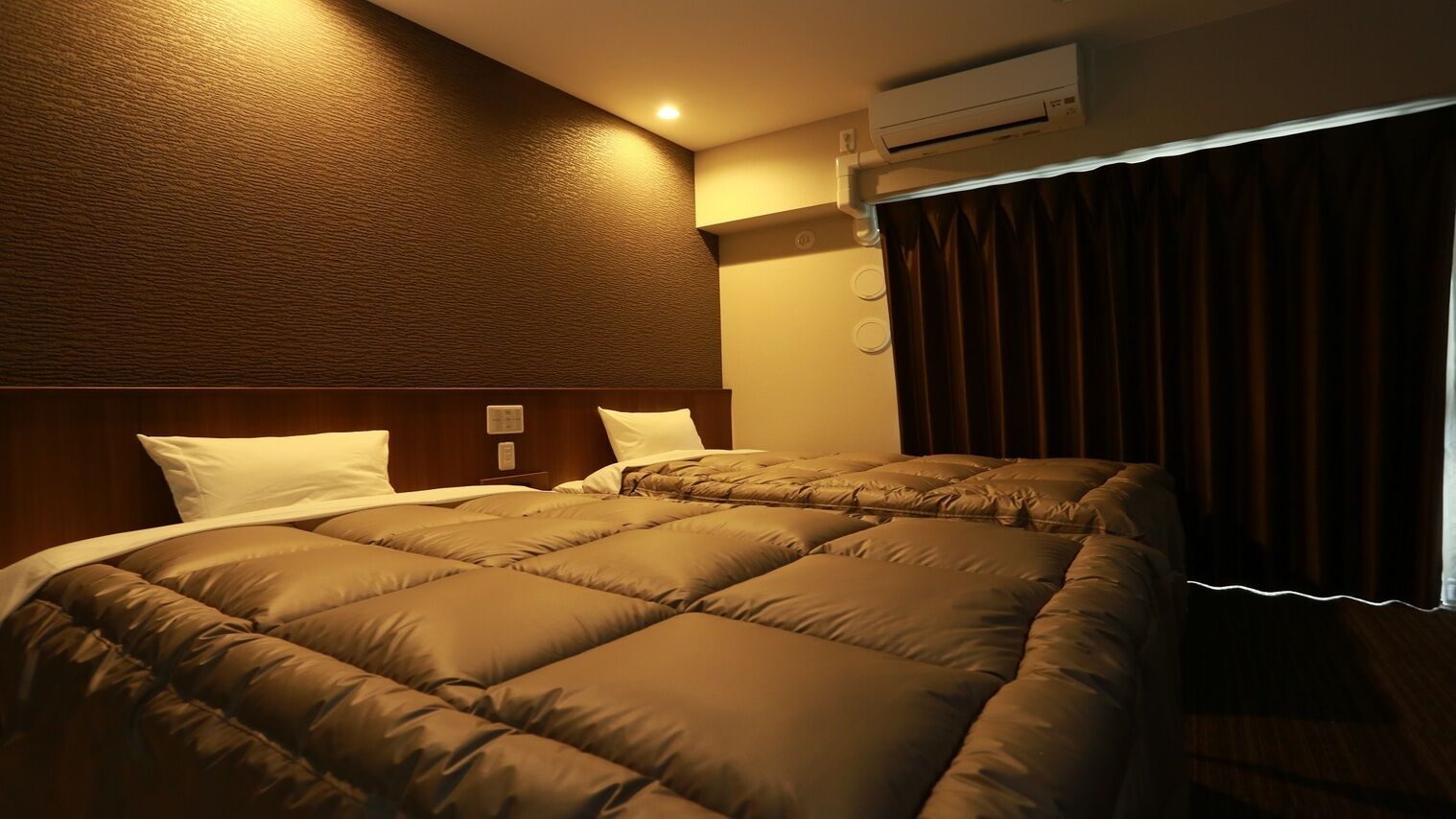 A hotel room with a large bed, an air conditioning unit, and a window with curtains.