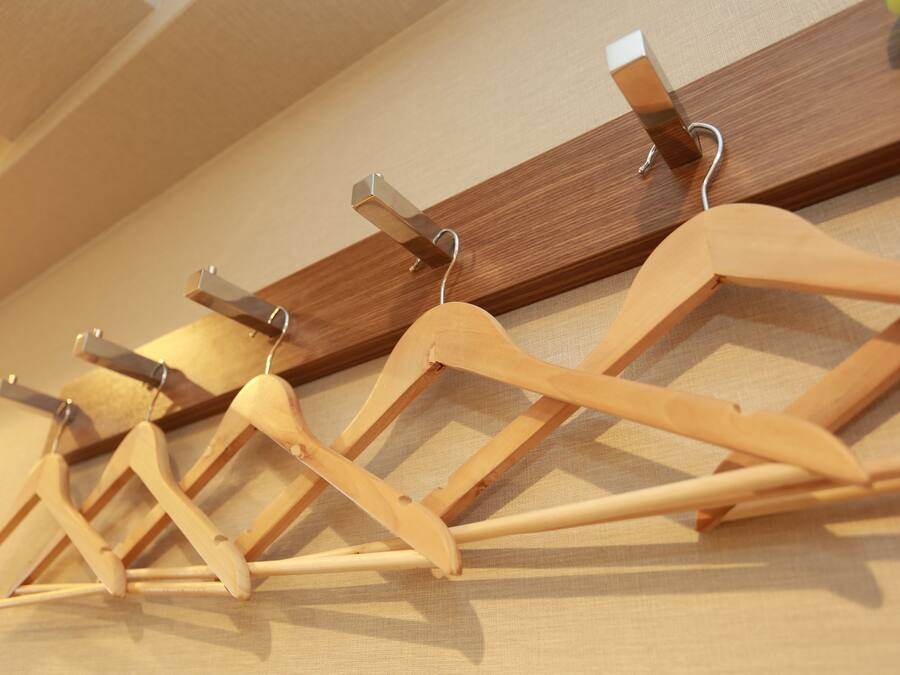 A wooden drying rack with metal clips against a beige wall.