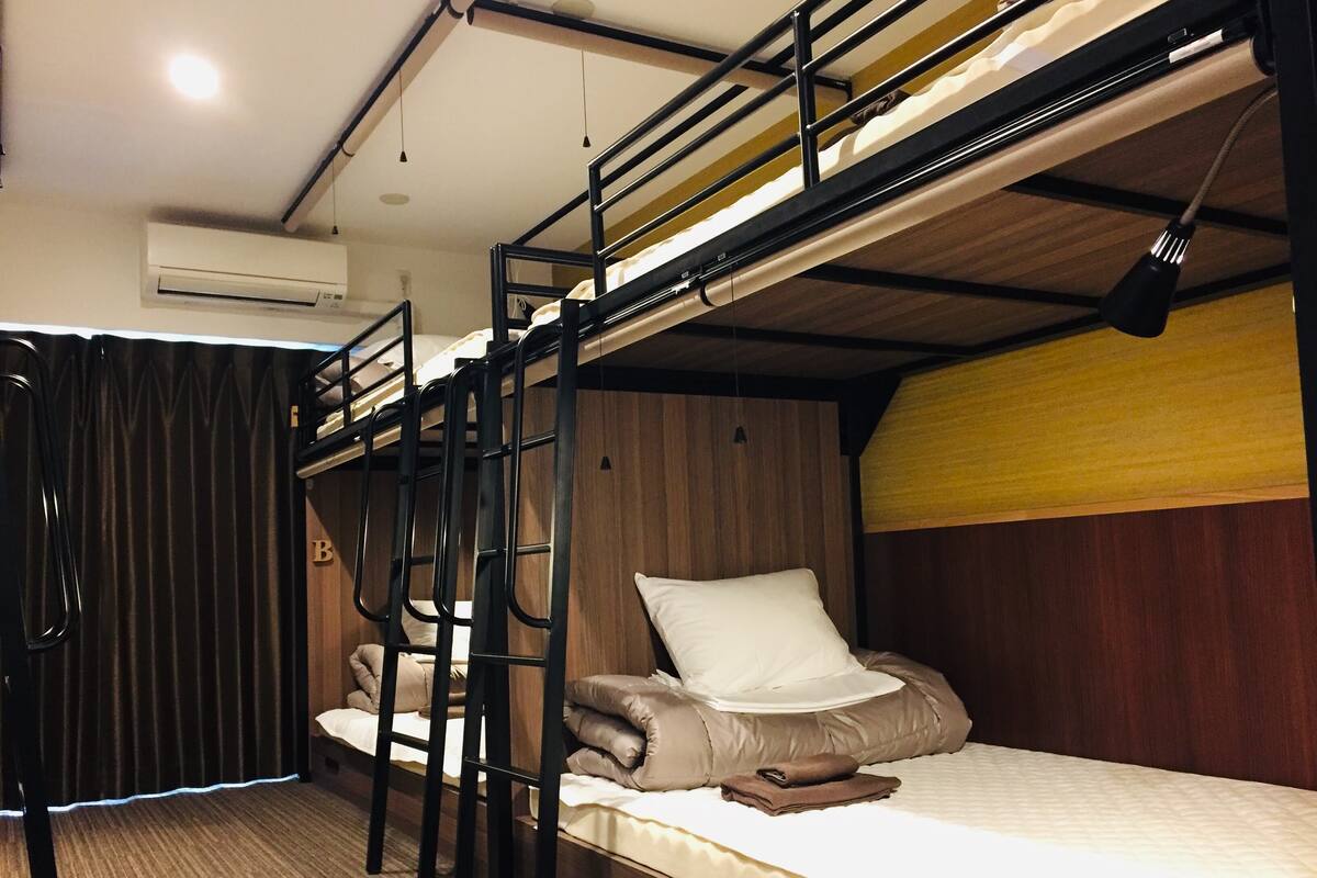 Een slaapkamer met een stapelbed, een houten hoofdbord, een klein tafeltje en een gordijn.