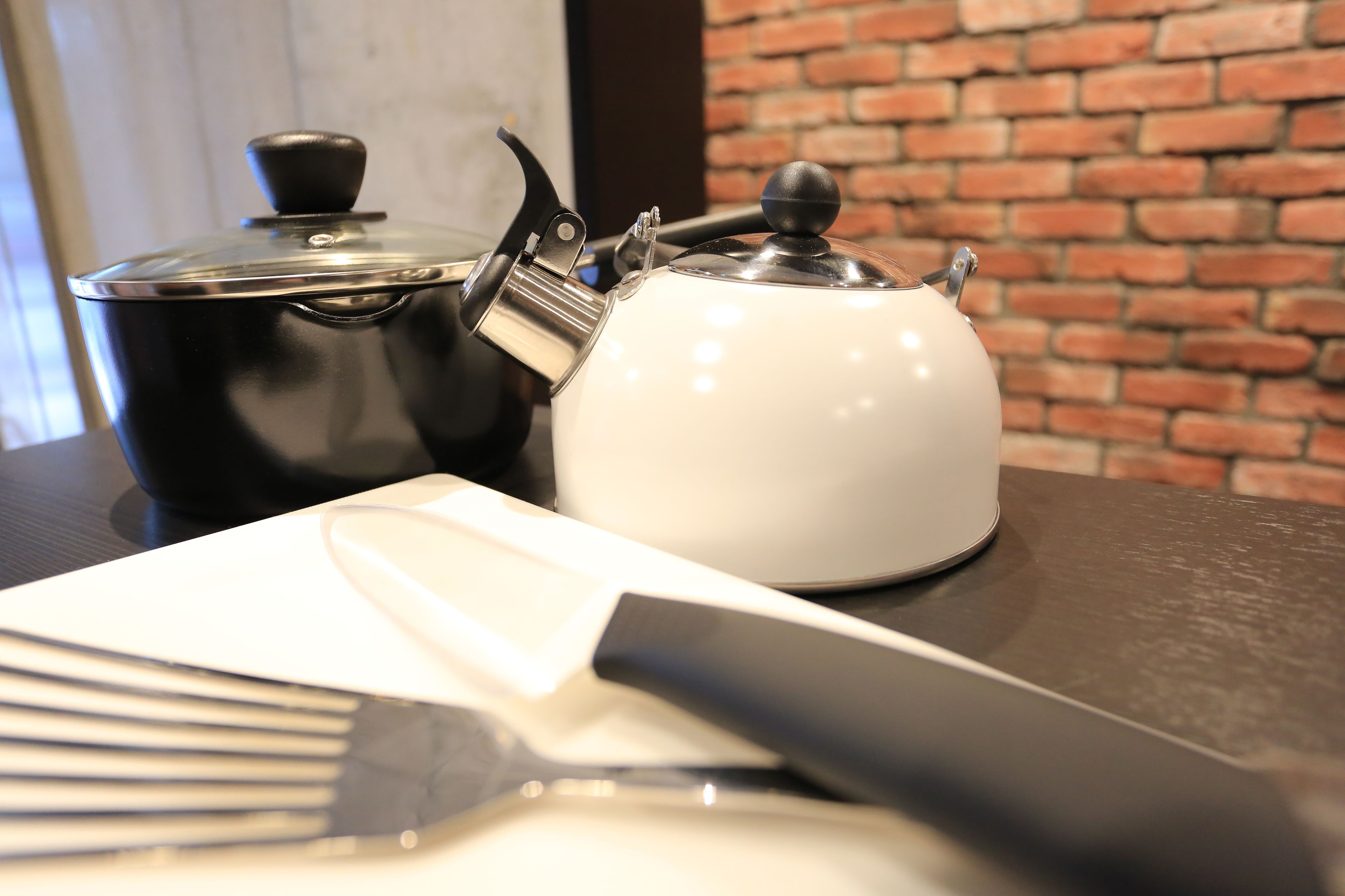 Una cocina con una tetera blanco y negro, un cuchillo y un tenedor sobre una mesa.
