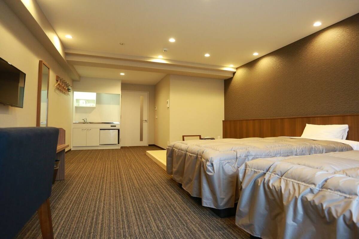 Een hotelkamer met twee bedden, een bureau, een stoel, een televisie en een kitchenette.