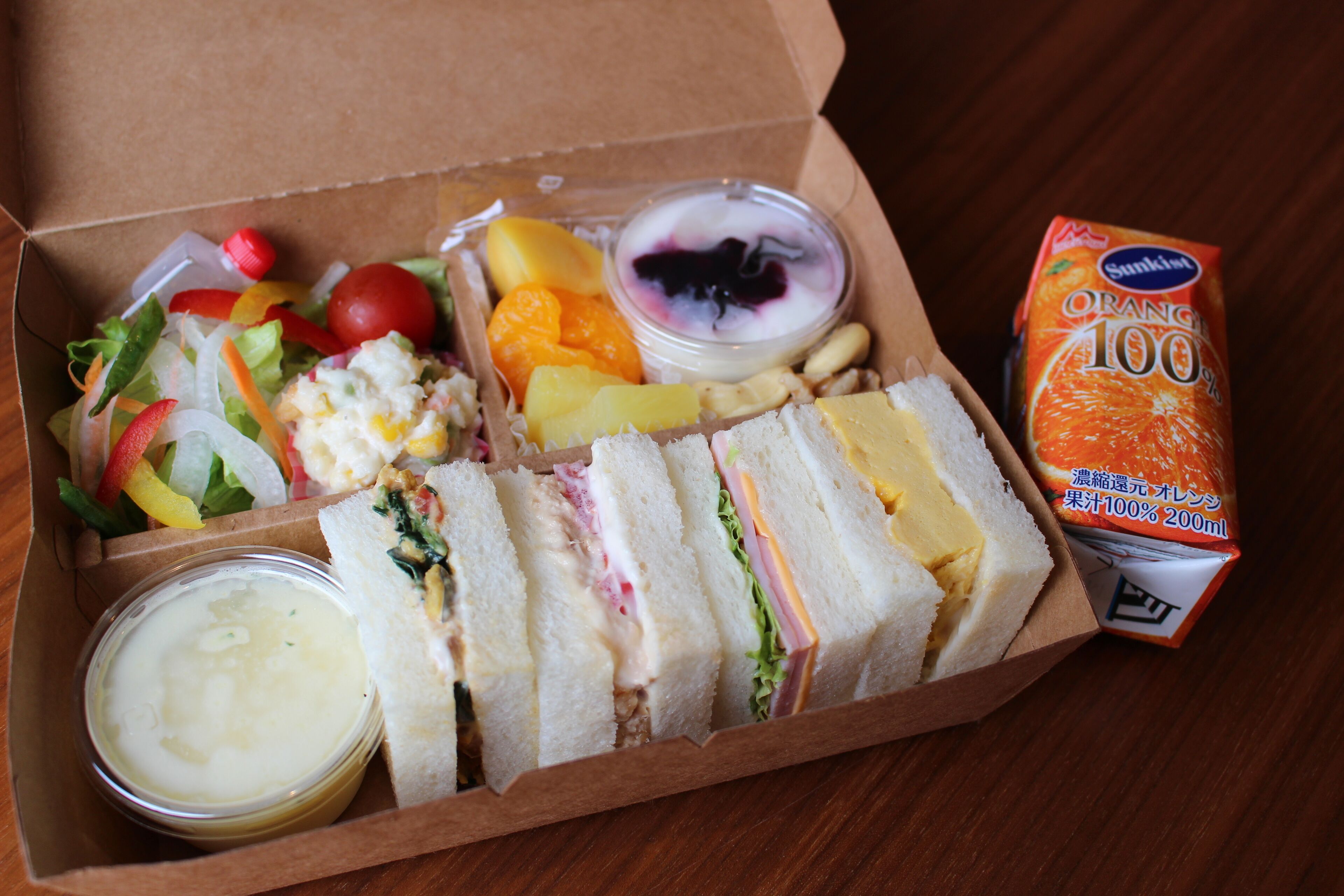 A box containing a sandwich, salad, fruit, yogurt, and juice.