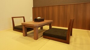 Quarto com mesa de madeira, duas cadeiras, um pequeno armário de madeira e piso de esteiras de tatame.