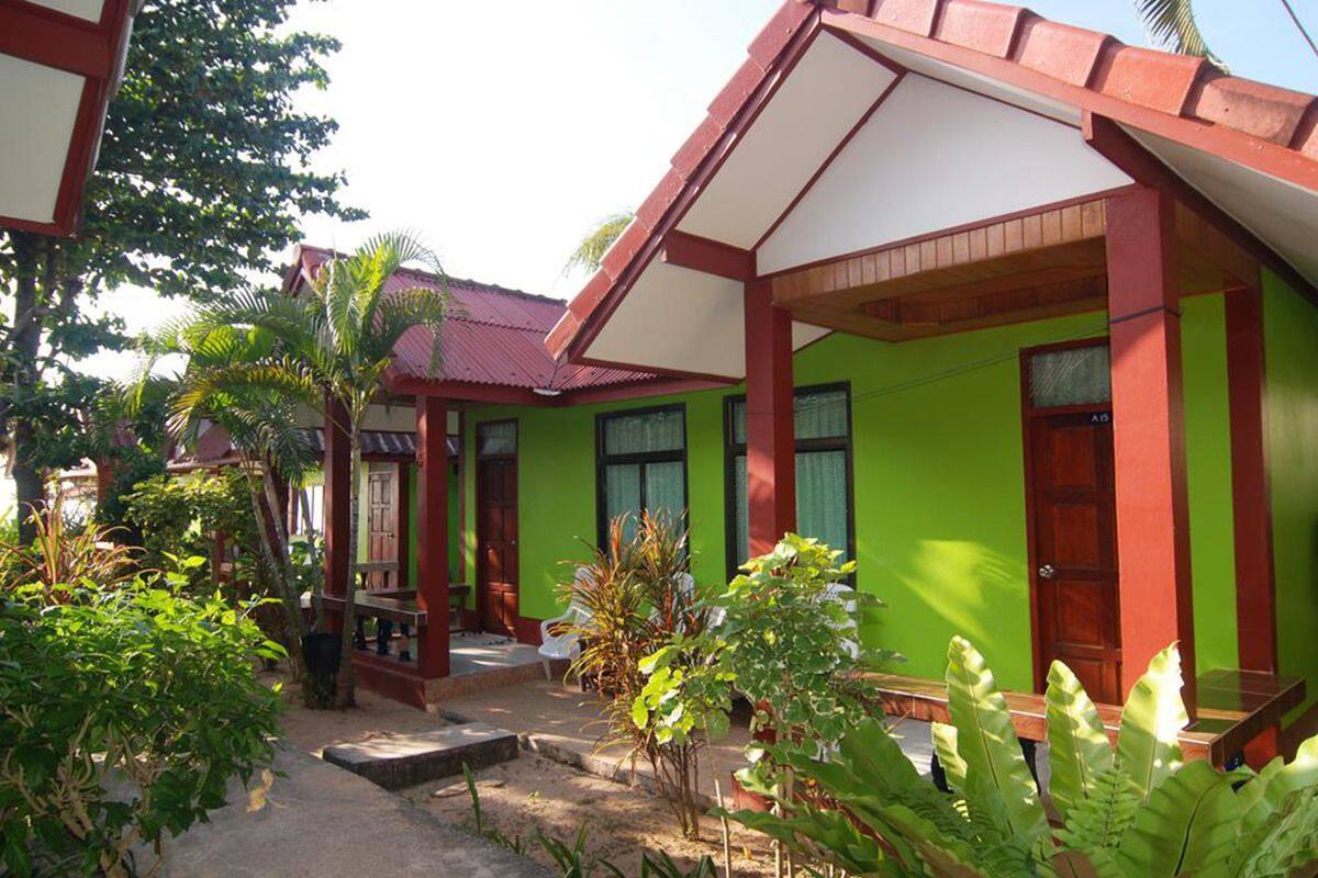 A two-story building with a green exterior and red accents, featuring a covered porch and a small garden area.