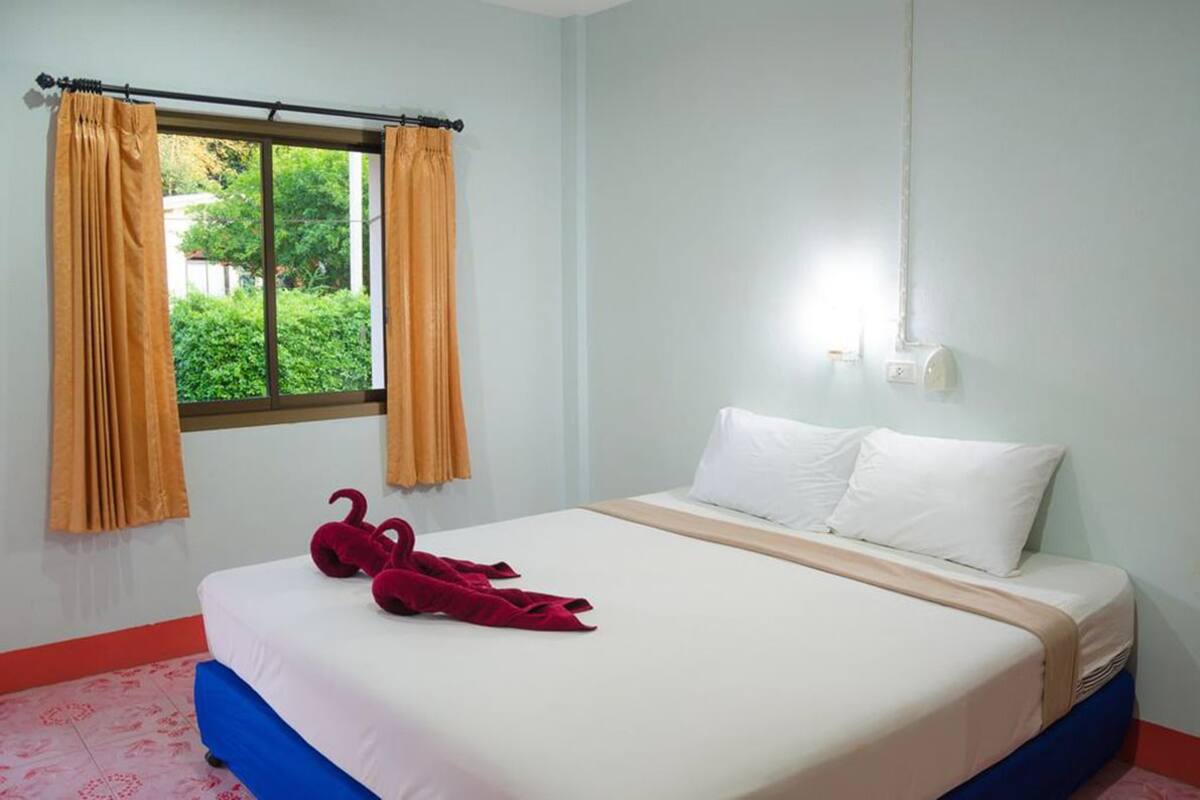 A hotel room with a bed, two white pillows, a red bathrobe, and a window with curtains.