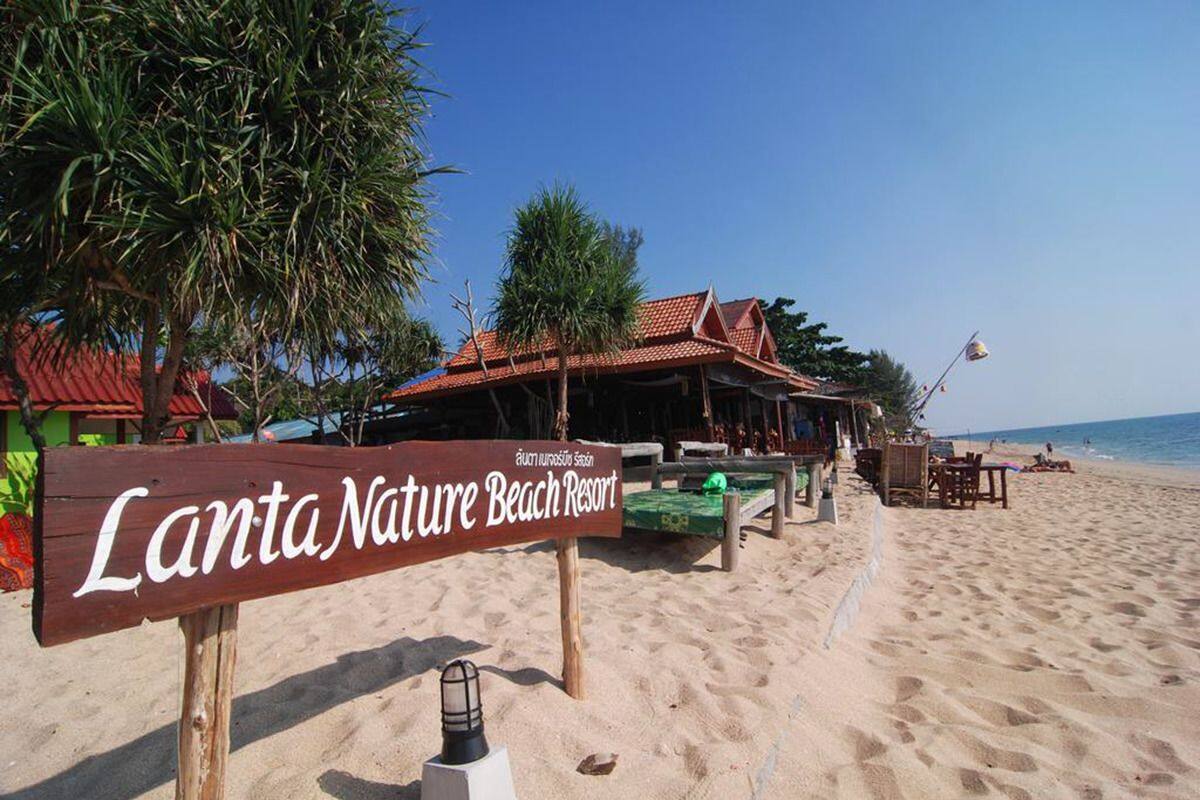 A beach resort named Lanta Nature Beach Resort with a signboard, beach chairs, tables, and a beach area.
